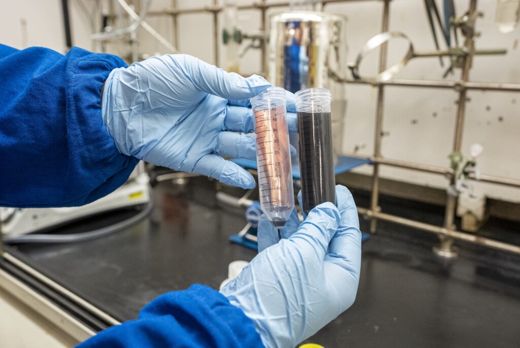 Links: een flesje met daarin een stroomcollectorkoperfolie van een batterij die na het oplossen van de Quick-Release Binder volledig is ontdaan van waardevolle elektrodecomponenten. Rechts: een flesje waar het bindmiddel actief oplost in alkalisch water. Foto: Marilyn Sargent, Berkeley Lab